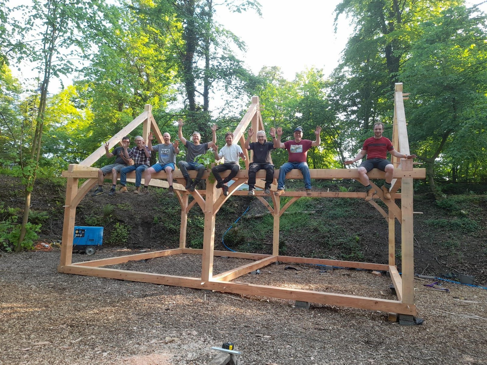 Timber framing course group celebrating after raising a traditional timber frame at Tree Tops and Train Tracks in North Wales