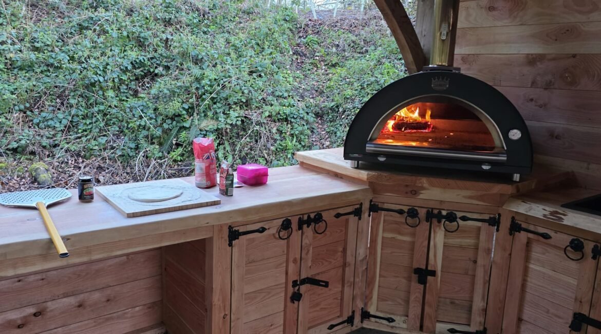 Wood-fired pizza oven and food preparation area in the covered communal kitchen at our woodland campsite in North Wales