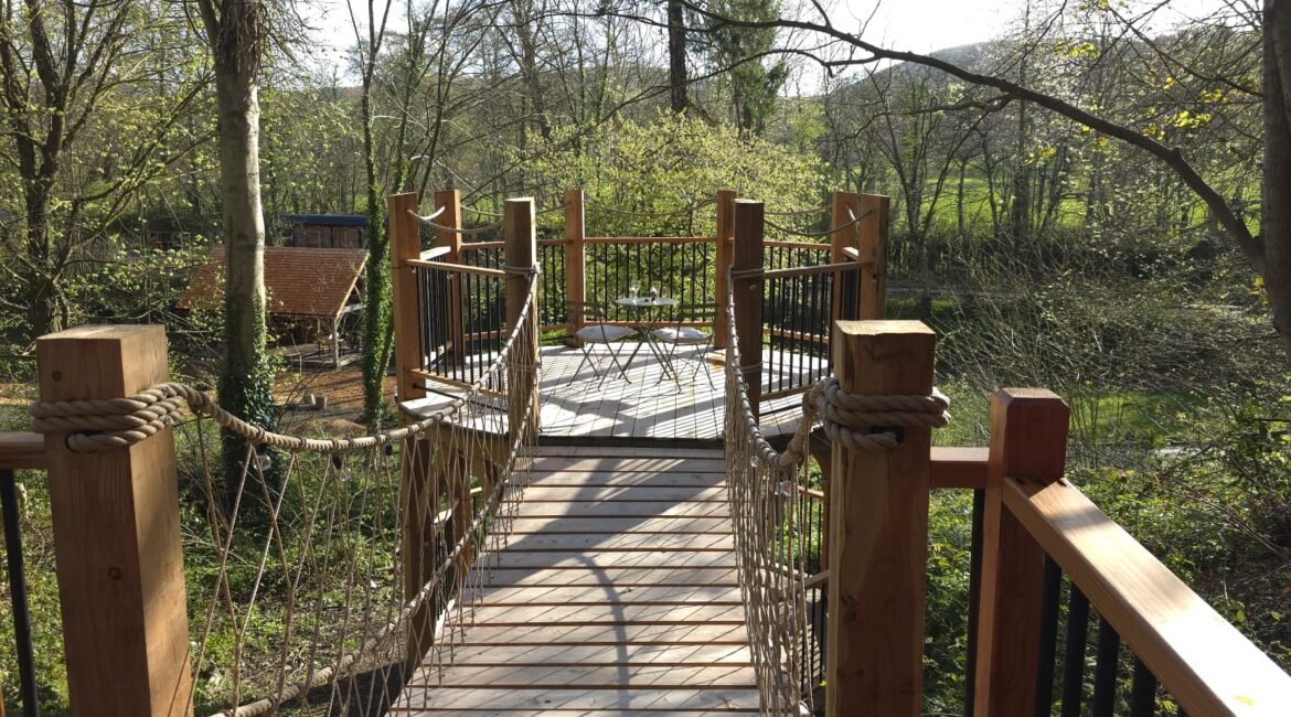 Rope bridge leading to a private woodland viewing deck at Toad Hideout glamping cabin, Tree Tops and Train Tracks, North Wales