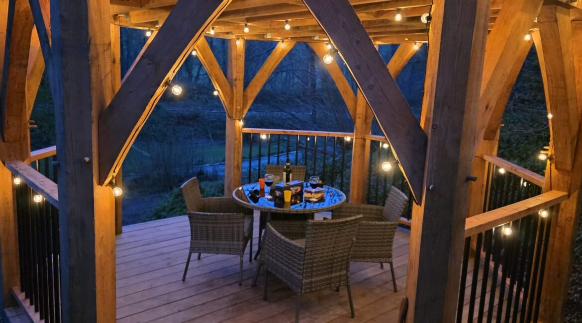 Covered outdoor dining deck with fairy lights surrounded by woodland at a unique glamping retreat in North Wales