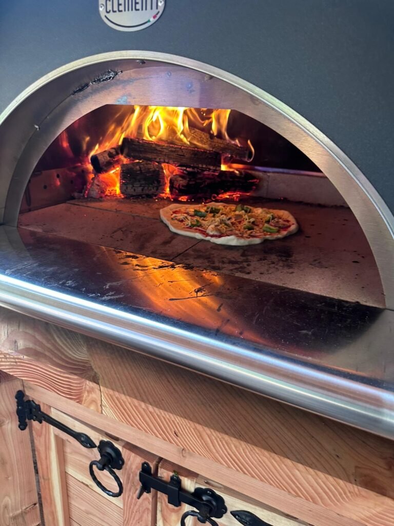Photograph of a pizza oven with a pizza cooking at Tree Tops and Train Tracks