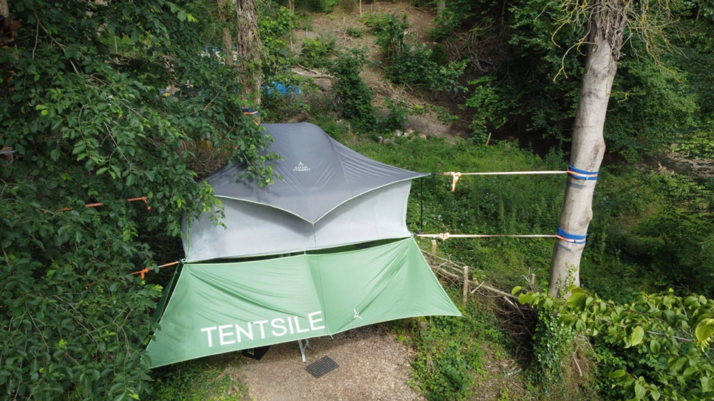 Tentsile tree tent set up between trees with rainfly, suspended above the ground for elevated forest camping.