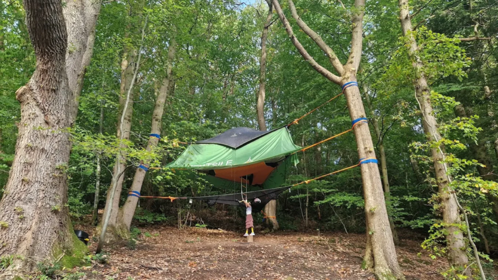 Three Tentsile Tents stacked upon one another between the trees in the woodland with ladder and rainfly.